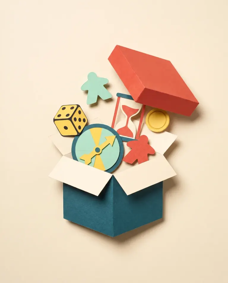 Cut paper collage: an open game box with a die, a spinner, an hourglass and a coin
